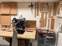 Radial arm saw mounted on plywood workbench with templates on wall