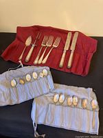 Overall layout of flatware on red and gray cloth roll showing all spoons, forks, knives and serving pieces