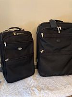 Front view of two black rolling suitcases with multiple zippered pockets and carrying handles.