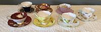 Seven tea cups with matching saucers displayed in a row showing various colors and patterns.