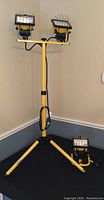 Full view of yellow adjustable tripod with two halogen lights mounted and separate single halogen light on floor.