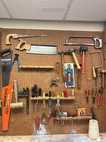 Photo of pegboard holding diverse woodworking hand tools including saws, pliers, hammers, screwdrivers, and squares arranged organized by type.