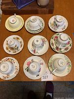 Nine fine china tea cups and saucers displayed upside down on a wooden surface showing floral designs and gold rims