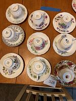 Nine bone china tea cups resting upside down on their matching saucers on a wooden table. Each set features unique floral patterns and gold trim.