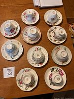 Photo of all ten china teacups and matching saucers arranged upside down on a wooden table showing various floral designs and gold trim.