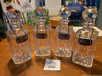 Full view of the four crystal decanters with multi-faceted stoppers on a wooden table.