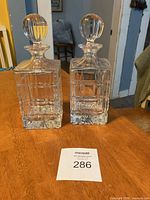 Front view of the twin column cut crystal decanters with stoppers placed on a wooden table.