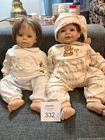 Two vinyl collector dolls sitting side by side on couch.