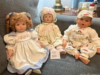 Photo showing three 19 inch vinyl dolls, one boy and two girls seated on a couch, dressed in detailed period-style clothing.