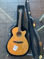 Full view of acoustic guitar seated in open black hardshell case on tiled floor