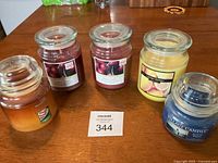 Five glass jar candles displayed on table with visible labels and wax. Seller's lot number and sticker included in photo.