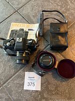 Minolta XE-7 camera body with attached Tiffen 80mm lens, flash unit in leather pouch, and owner's manual on tiled surface.