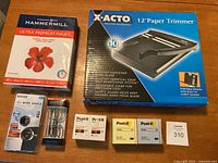 Overview of all items including boxed paper trimmer, paper ream, reading glasses, lens, and Post-it notes.
