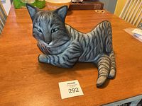 Reclining gray tabby cat sculpture on wooden table with auction lot number card.