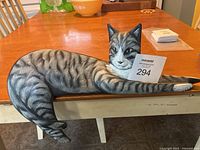 Full side view of the elongated reclining gray tabby cat sculpture on a table, showing body posture and fur detail.