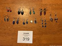 Nine pairs of assorted sterling silver earrings arranged on wood surface with auction lot card