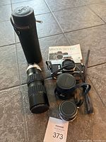 Full view of camera, lenses, manual, and lens case arranged on tiled floor