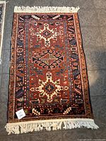 Full view of the vintage wool carpet showing overall design and fringed edges on tile floor.