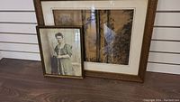 Lot showing two framed artworks: a smaller portrait of a lady and a larger framed landscape painting beside it