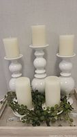 Three tall white ceramic candle holders with round bulbous bases and a white pillar candle on each.