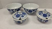 Two white ceramic rice bowls and two matching sauce bowls with lids, all decorated with blue floral design.