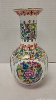 Front view of porcelain Chinese vase showing colorful floral patterns and gold trim on a white background.