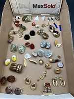 Full lot displaying an assortment of vintage and modern earrings and rings on a cardboard surface.
