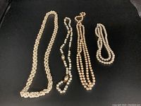 Four faux pearl necklaces laid out on dark surface showing their lengths and bead variation