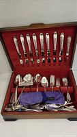 Full view of wooden box with red velvet lining holding assorted silverplate cutlery pieces including forks, spoons, and specialty utensils.