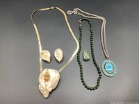 Full set showing all four jewelry pieces: large white pendant necklace with matching earrings, jade bead necklace with green stone pendant, and blue stone necklace with one missing stone.