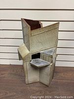 Front view showing the angular and geometric architecture of the pottery umbrella stand with varying shades of beige and gray.