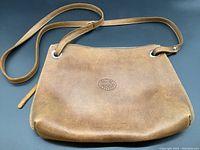 Front view of brown Roots leather purse with embossed logo and shoulder strap