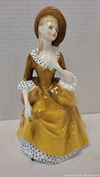 Front view of the Royal Doulton Sandra figurine showing detailed facial features and front of yellow dress with white and black spotted trim.
