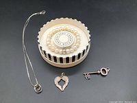Top-down view showing entire lot: silver necklace with rings pendant, winged heart pendant, key pendant, and pearl bracelet in box.