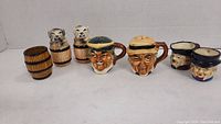 Six Toby style ceramic items arranged in a line: two barrel-shaped shakers on left, two character heads (salt and pepper) in middle, two small Toby style cups on right, all about 2-3 inches high.