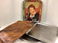 Photo of all four trays together showing size differences and materials: Coca Cola metal tray, wooden tray, silver metal tray, round metal tray