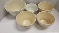 Five ceramic mixing bowls of varying sizes with cream/off-white glaze, showing surface crazing and discoloration.