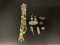 Overview of the lot showing necklace, earrings, pins, and brooches on a black background.