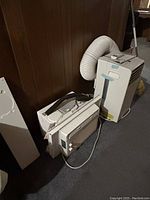 Two posed air conditioning units, one portable with vent hose and front louvers, second standard window type unit nearby.