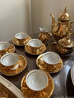 Full view of the gold teapot set including six teacups and saucers arranged on a dark surface.
