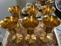 Six gold wine goblets on the two-tone serving tray shown from above, highlighting the smooth finish and shape.