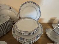 Various octagonal plates with pastel geometric border stacked beside saucers and cups.