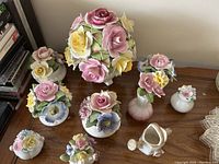 Collection of varied ceramic flower bone china figurines in pastel colors displayed on a wooden surface.