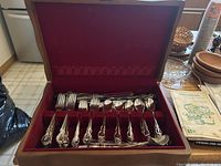 Wooden box open showing the complete flatware set including forks, spoons, knives, and serving utensils