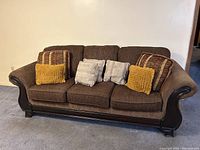 Brown fabric 4-seater lounger couch with wooden armrests and base, shown with six decorative throw pillows
