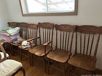 Photo showing six matching wooden dining chairs with carved backrests and vertical slats, including two armchairs with armrests.