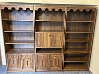 Front view of three wood veneer bookshelves with multiple shelves, two lower cabinets on outer bookshelves, and central drop-down door cabinet on middle bookshelf