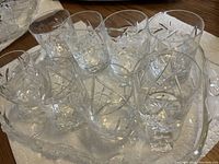 Eight pinwheel pattern crystal scotch glasses arranged on a rectangular crystal tray on a table.