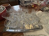 Photo showing a large group of clear crystal wine glasses with pinwheel cut designs arranged on a rectangular stainless steel tray on a surface.