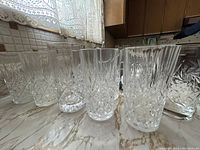 Side view showing multiple tall crystal tumbler glasses arranged on a marble countertop, highlighting their pinwheel cut design.